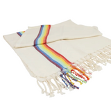 An off-white woven blanket with a vibrant rainbow stripe down the center and matching fringed tassels, displayed on a clean white background.