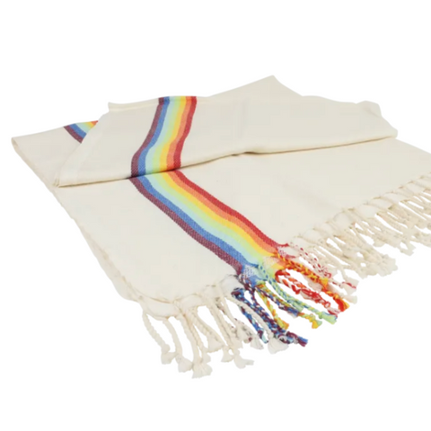 An off-white woven blanket with a vibrant rainbow stripe down the center and matching fringed tassels, displayed on a clean white background.