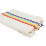 A folded cream-colored woven throw blanket with a vibrant rainbow stripe pattern and fringed edges, shown on a plain white background.