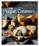 The Vegan Creamery book cover by Miyoko Schinner, featuring a rustic cheese board with various vegan cheeses, figs, and a small bowl of dip on a dark textured background.
