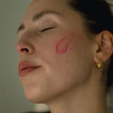 Close-up of a face with pink rose dew moisturizer on cheek, wearing a gold earring.