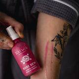 Person holding a pink bottle labeled 'Rose Dew' 