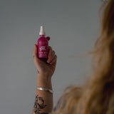 Person holding a rose dew bottle against a gray background